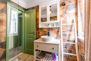 Un baño con una puerta verde, un lavabo blanco con un espejo encima y un estante con artículos de tocador.