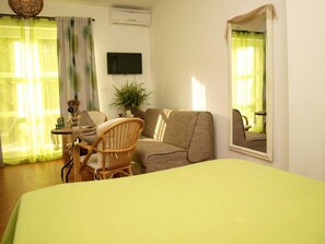 Una habitación con cama, sofá, sillón, una mesita y una planta en maceta.