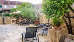 Eine Außenpatio mit Steinböden, Metallstühlen und -tischen. Im Hintergrund ist ein großer Topfpflanze und eine Steinmauer zu sehen.