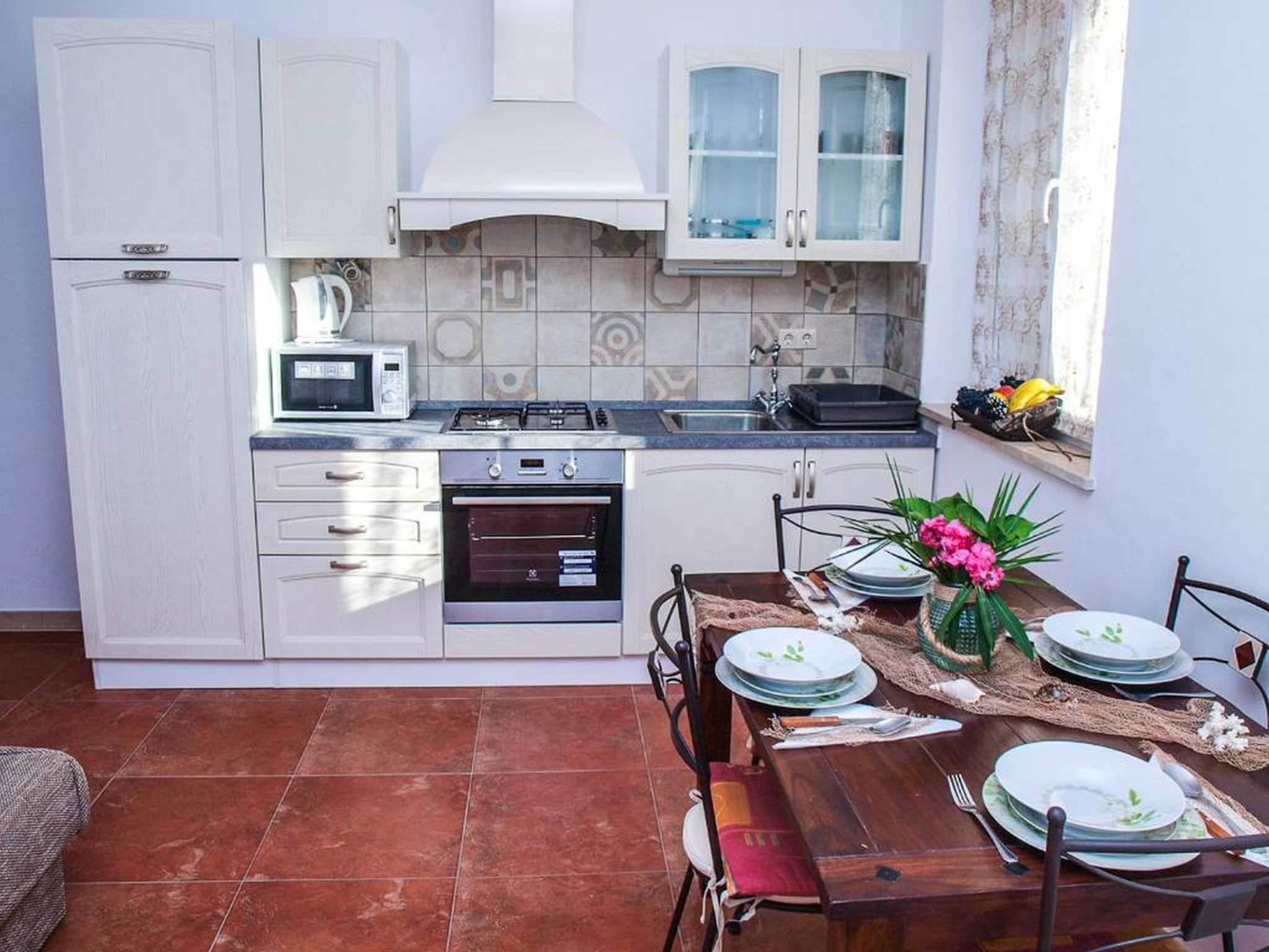 Une cuisine compacte avec des meubles blancs, un four à micro-ondes, un four traditionnel et une cuisinière à gaz.