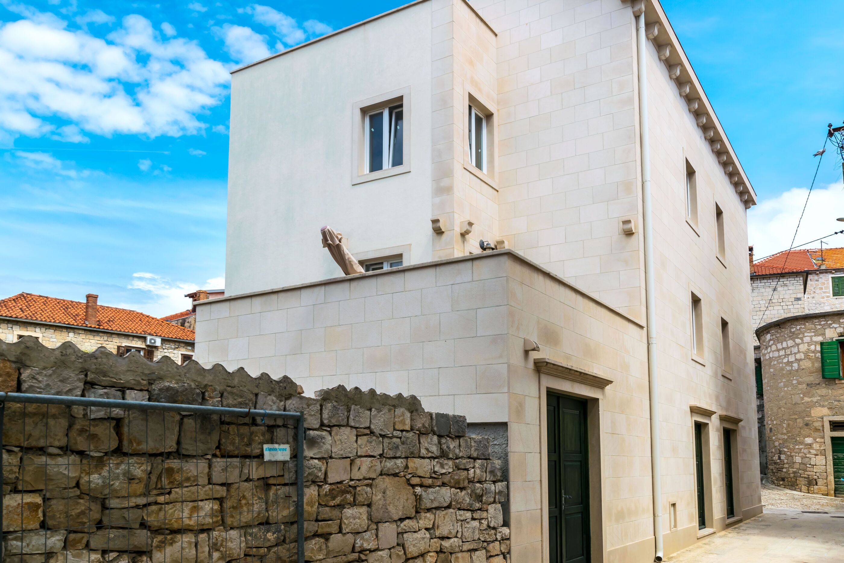 A two-story building with a stone wall in front, a door, and windows.