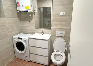 Une petite salle de bain équipée d’un lave-linge, d’un lavabo et de toilettes.