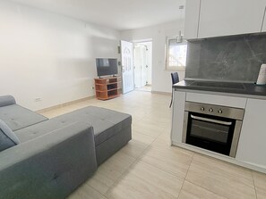 Una cocina moderna con horno empotrado, un sofá gris y un televisor sobre un soporte de madera.