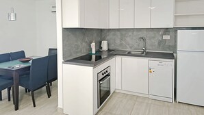 A modern kitchen with white cabinets, a built-in oven, a stainless steel sink, and a compact refrigerator. - Apartments Helen (Rogoznica)