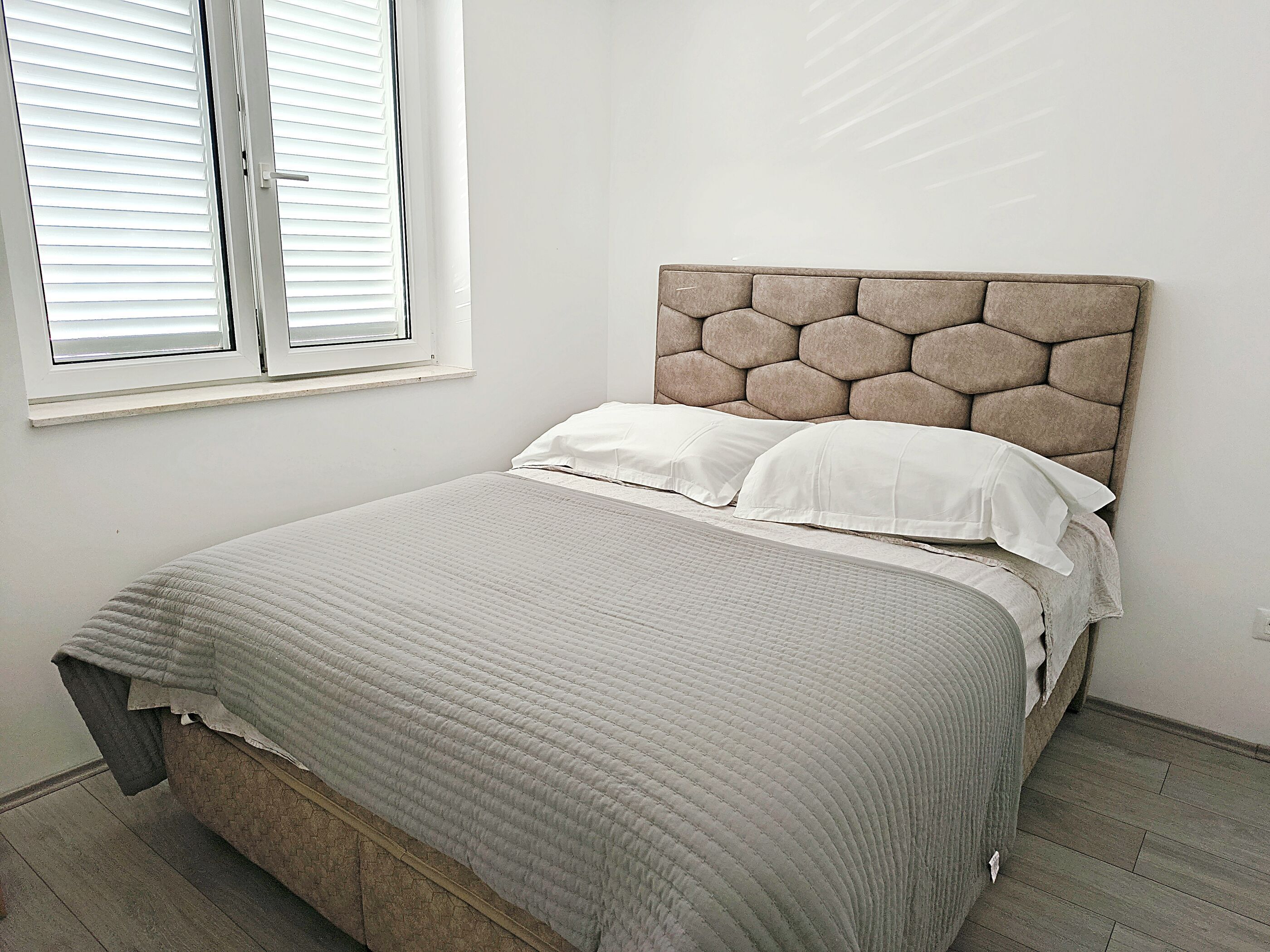 A bedroom with a bed, a window with blinds, and a plain wall.