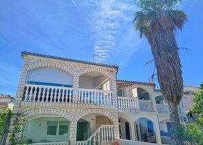A two-story building with a balcony, a staircase, and a palm tree. - Apartments Helen (Rogoznica)