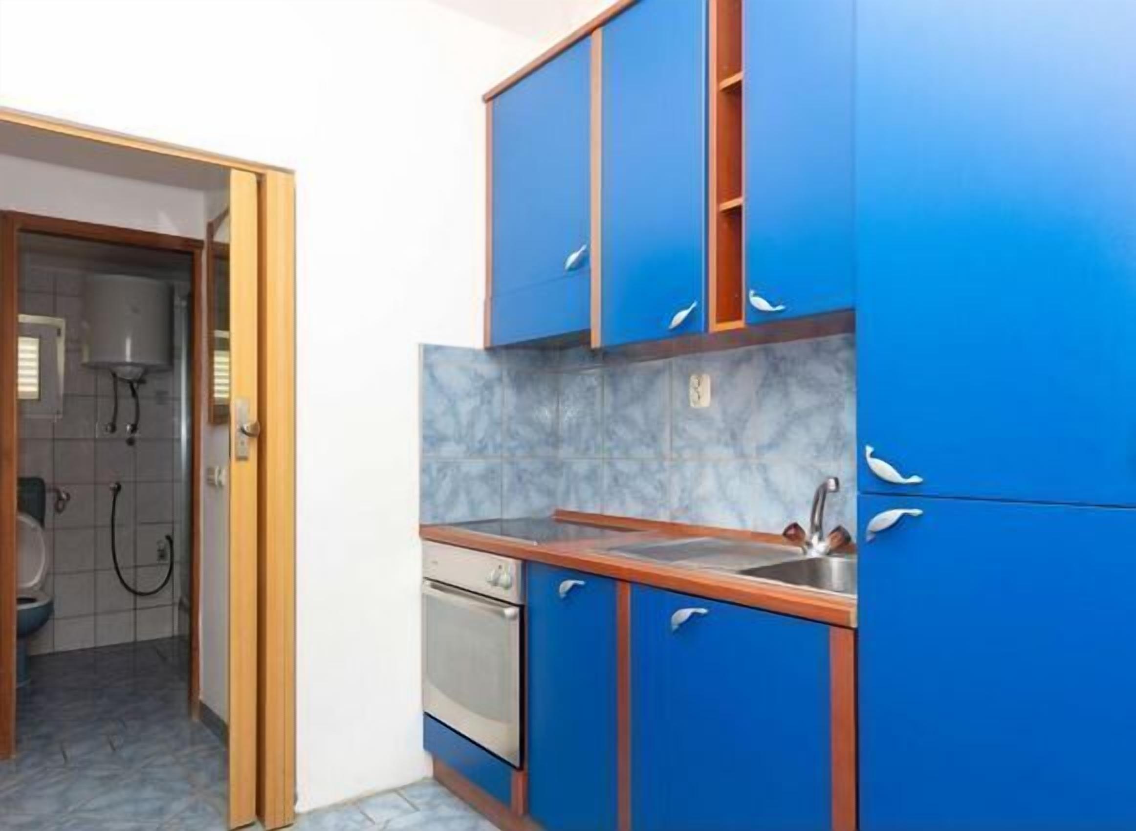 A kitchen with blue cabinets, a stainless steel sink, and a marble backsplash.