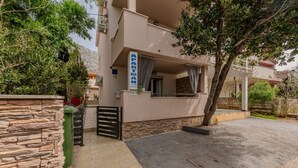 A modern apartment building with a stone facade, a balcony with curtains, and a paved driveway. - Apartments Mil (Karlobag)