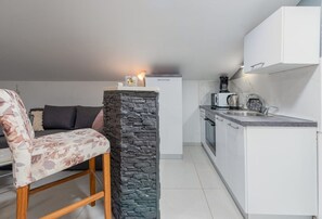 Eine kompakte Küche mit weißen Schränken, einer Wand mit Steinverkleidung und einem Essbereich mit einem Blumenstuhl.