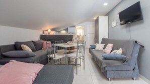 A modern living room with a grey sofa, a smaller grey couch, a dining table with chairs, and a flat-screen TV mounted on the wall. - Apartments Mil (Karlobag)