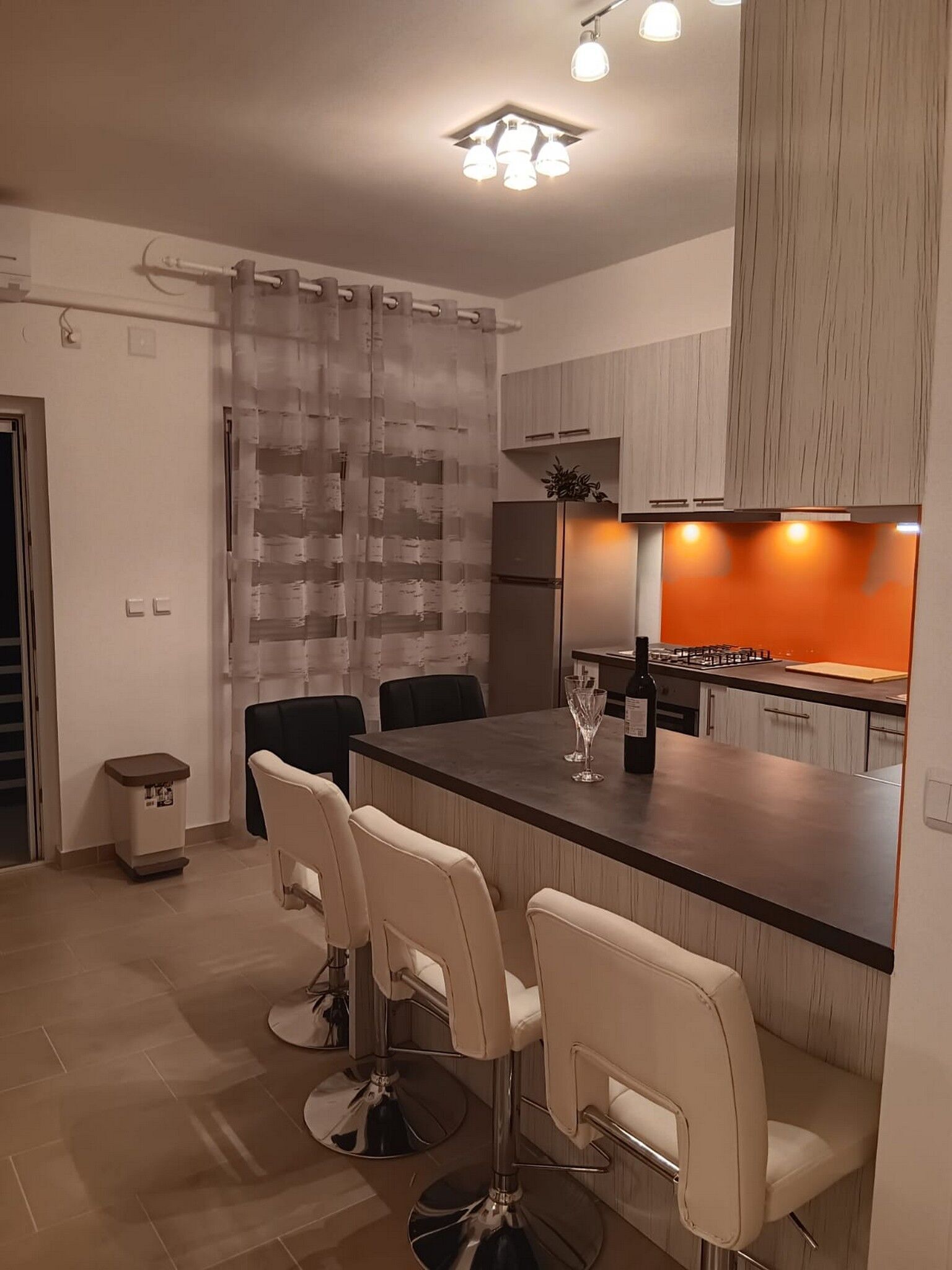 A modern kitchen with a central island, bar stools, and a dining area.