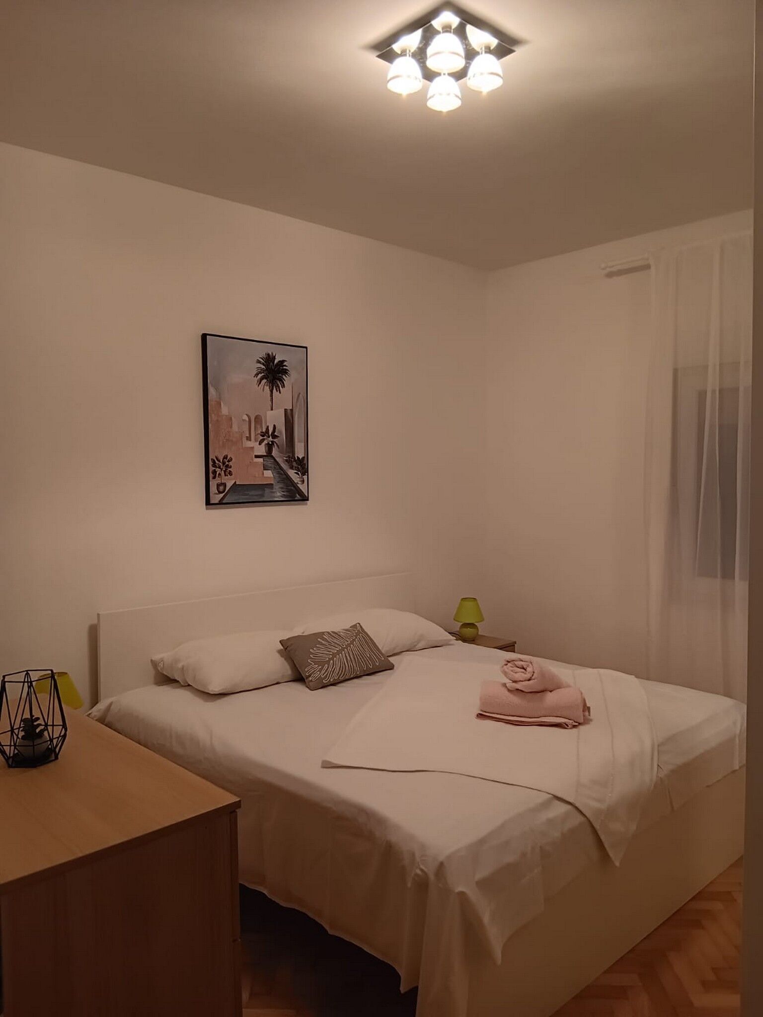 Une chambre à coucher bien rangée, avec un lit, une table de chevet, une lampe et un tableau accroché au mur.