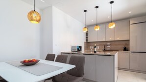 Una cocina moderna con una isla central, iluminación colgante y un comedor con mesa y sillas.