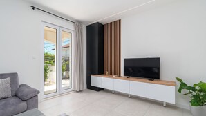 Una sala de estar moderna con un sofá gris, un mueble de televisión de madera y un ventanal con vistas a zonas verdes.