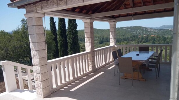An outdoor patio with a table and chairs, stone pillars, and a view of a forested landscape. - House Ule 2 (Korčula)