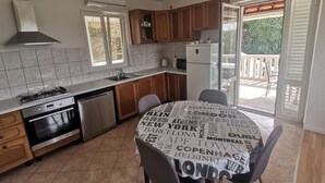 A modern kitchen with a gas stove, oven, dishwasher, and a sink. There is a dining table with a tablecloth featuring city names. - House Ule 2 (Korčula)