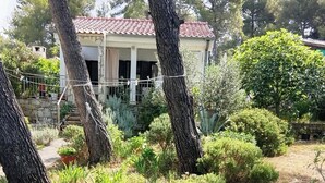 Un mur de pedra, una casa amb teulada ceràmica i vegetació als voltants.