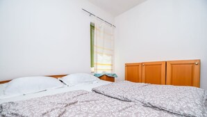 A bedroom with a double bed, two pillows, a wooden headboard, and a window with blinds. - Apartment Agi (Kastela)