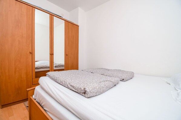A bedroom with a wooden wardrobe, a bed with grey floral bedding, and white walls. - Apartment Agi (Kastela)