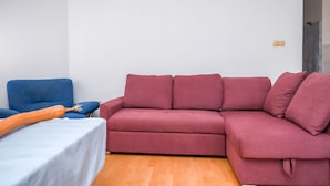 A living room with a red sectional sofa, a blue armchair, and a white table. - Apartment Agi (Kastela)