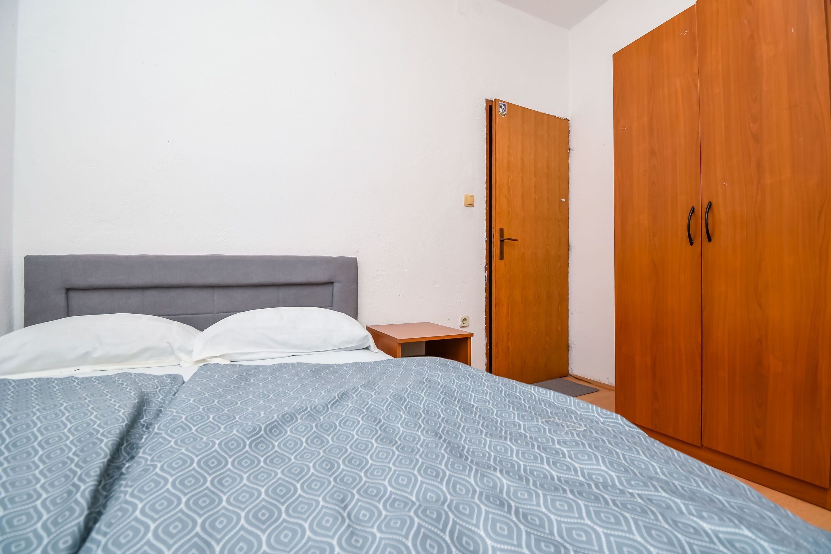 A bedroom with a bed, a wooden wardrobe, and a nightstand.