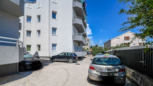 A parking area with two cars, a building with multiple windows and balconies, and a clear blue sky. - Apartment Agi (Kastela)