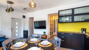 Egy modern étkező, melyben egy kerek, négy személyes asztal található, a falra szerelték egy síkképernyős televíziót, a konyhában pedig fekete szekrények és egy sárga színű, kiemelő fal adja a hangulatot.