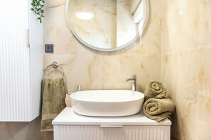 A bathroom with a round mirror, a white sink, and a towel rack. - Apartment Jasna (Supetar)
