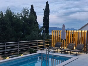 A pool area with lounge chairs, a wooden fence, and a view of trees and mountains. - Apartment Jasna (Supetar)