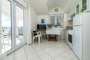 Una cucina compatta con angolo ristoro, TV e un balcone con sedie.