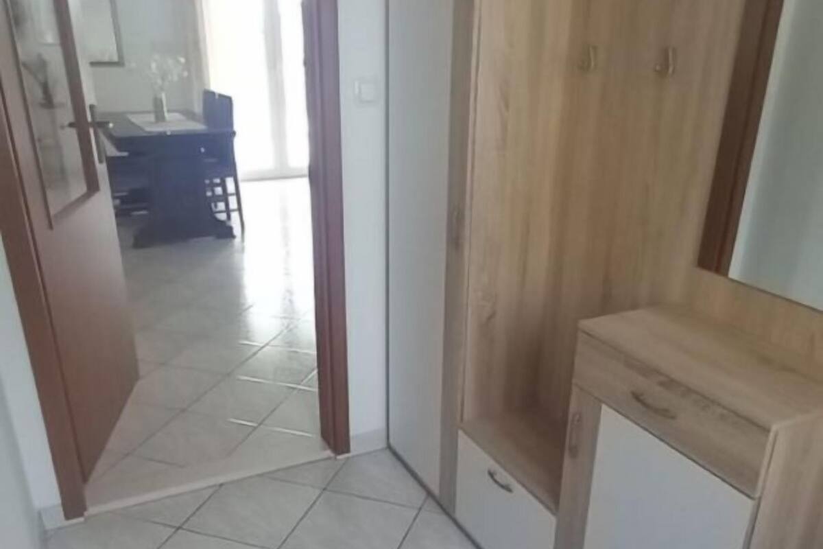 Un couloir au sol carrelé mène à une pièce où se trouvent une armoire en bois et un petit meuble.