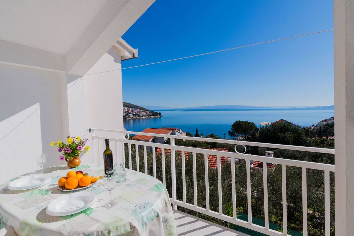 Un balcon avec une table dressée pour deux personnes, offrant une vue sur la côte.
