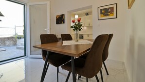 A dining area with a wooden table, brown chairs, a vase with flowers, and a kitchen in the background. - Apartments Kati (Seget)