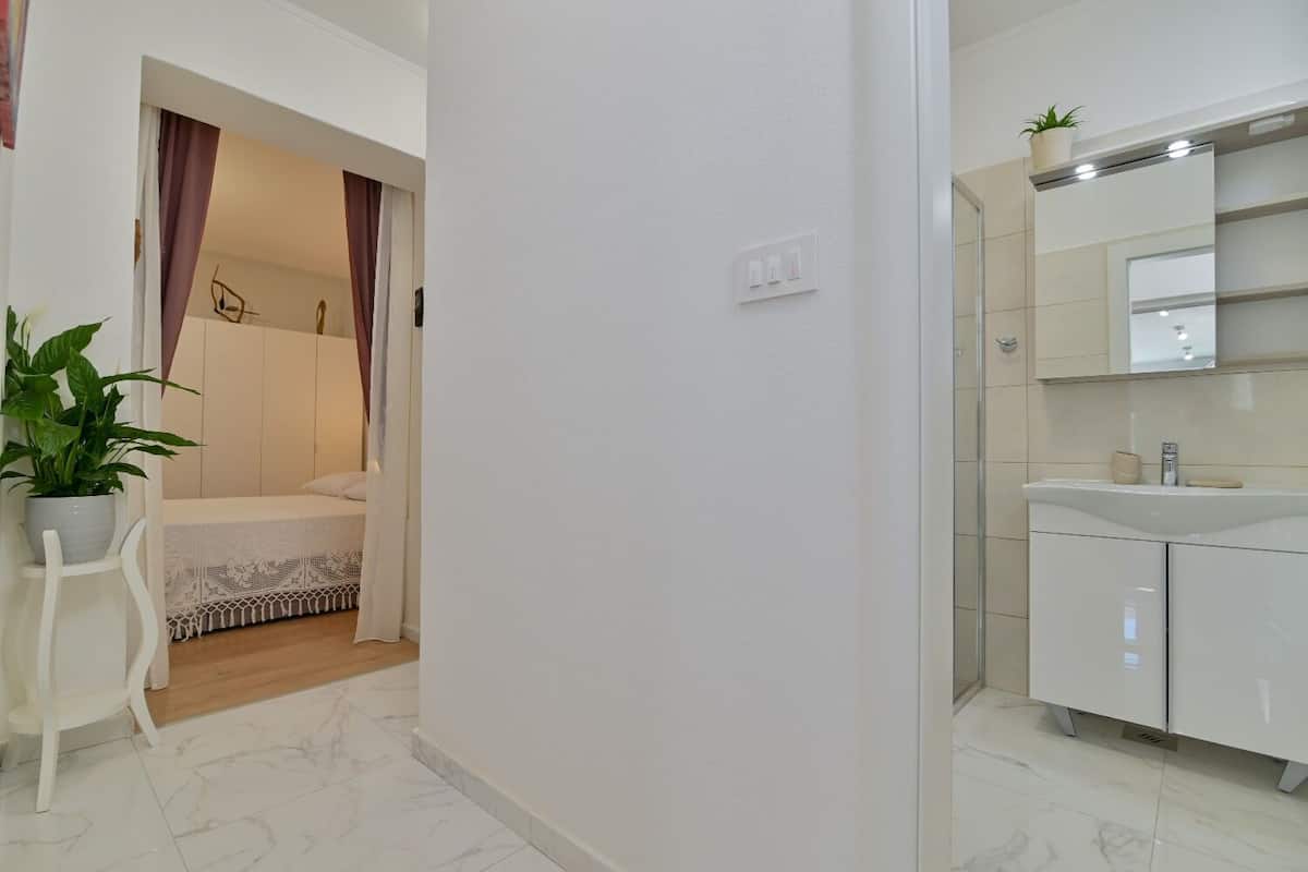 A modern bathroom with a white sink, mirror, and cabinets. There is a potted plant on the countertop.