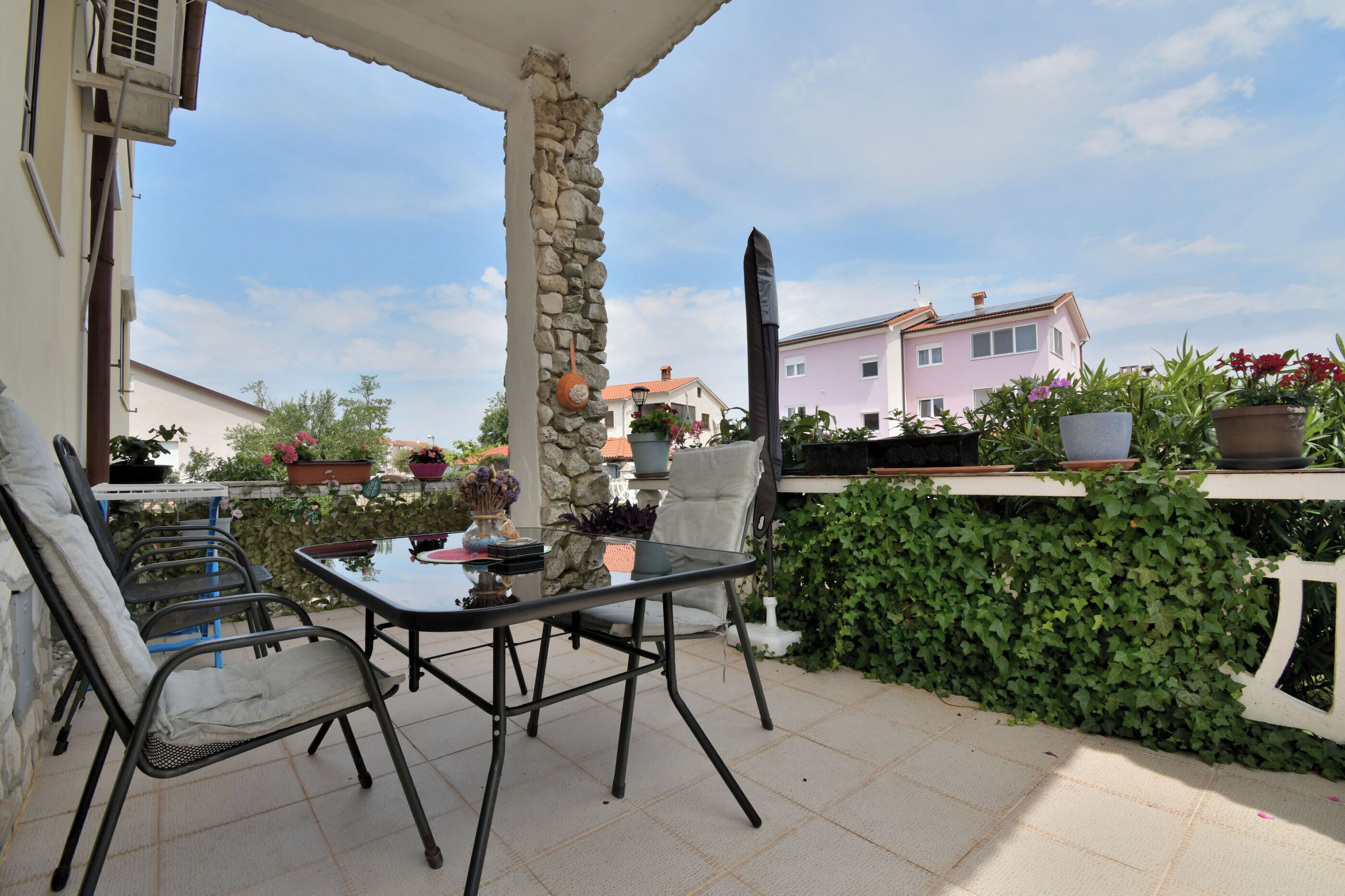 Una terrazza esterna con tavolo e sedie, un pilastro in pietra e piante in vaso.