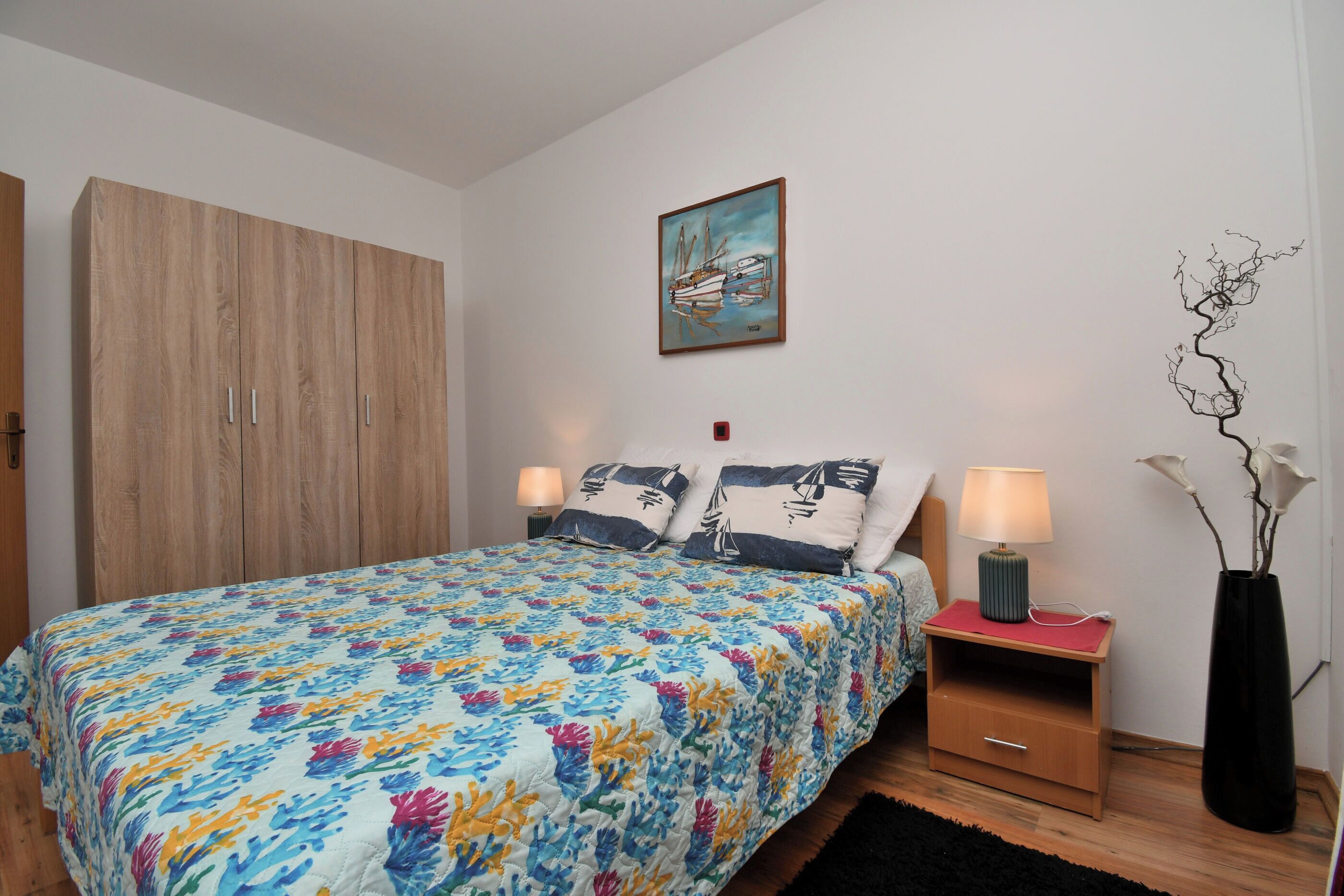 Une chambre à coucher avec un lit, une table de chevet, une lampe, un vase de fleurs et une armoire.