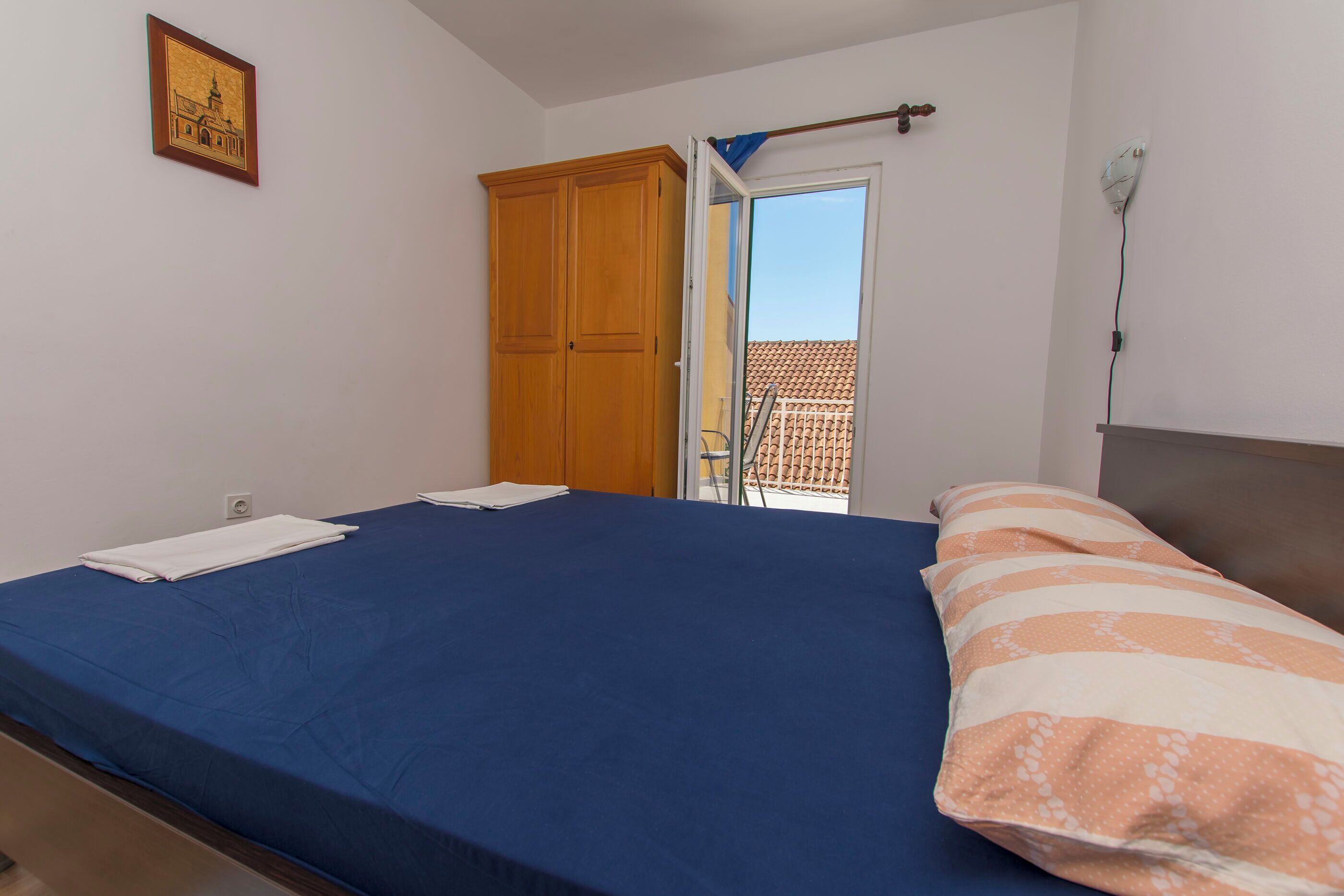 A bedroom with a bed, a wardrobe, a door leading to a balcony, and a wall-mounted light fixture.