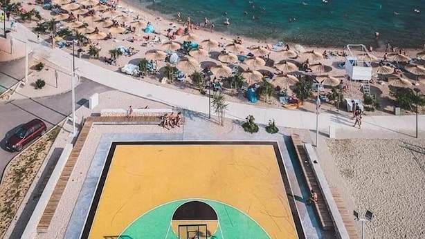 A basketball court adjacent to a beach with umbrellas and people. - Apartments Andrea (Sibenik)
