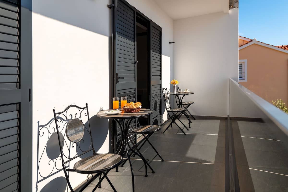 Un balcone con un tavolo apparecchiato per due persone, con un cesto di pane e un bicchiere di succo d'arancia.
