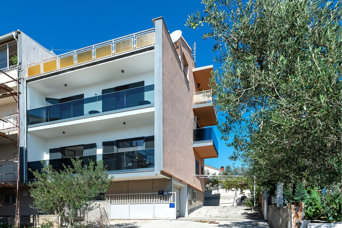 Un immeuble résidentiel à plusieurs étages, doté de balcons, d’une antenne parabolique et surplombant un ciel bleu dégagé.