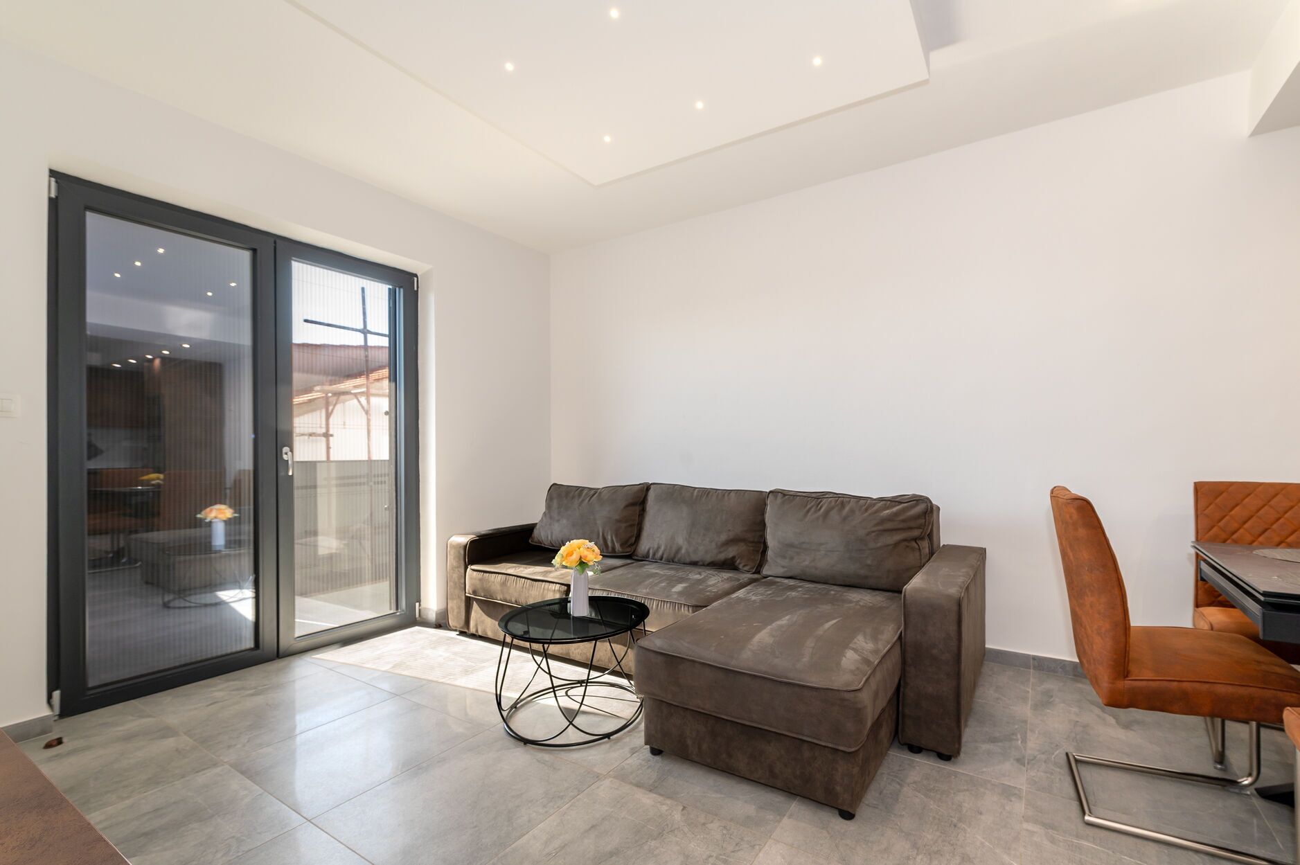 A modern living room with a grey leather sofa, a small black side table, and a brown leather chair.