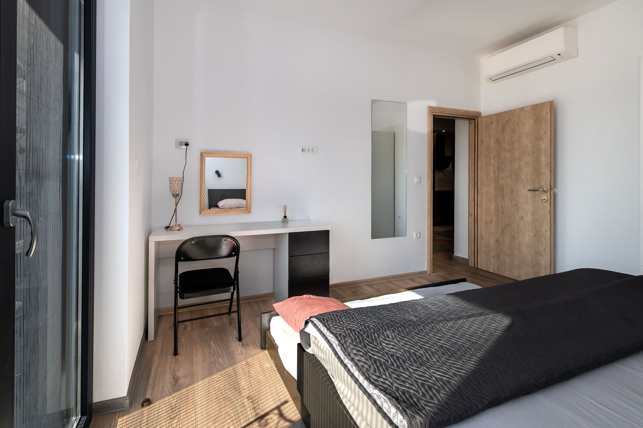 Ein Schlafzimmer mit einem Bett, einem Schreibtisch mit Stuhl, einem Spiegel und einem Kleiderschrank.