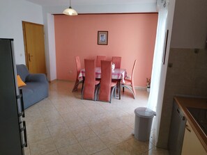 Ein Essbereich mit Tisch und Stühlen, einer Couch, einem Mülleimer und einer Tür.