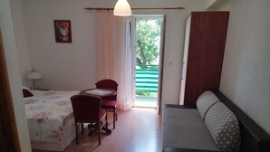 A room with a bed, a small table with chairs, a sofa, and a window with a view of greenery. - Apartments Mare (Brela)