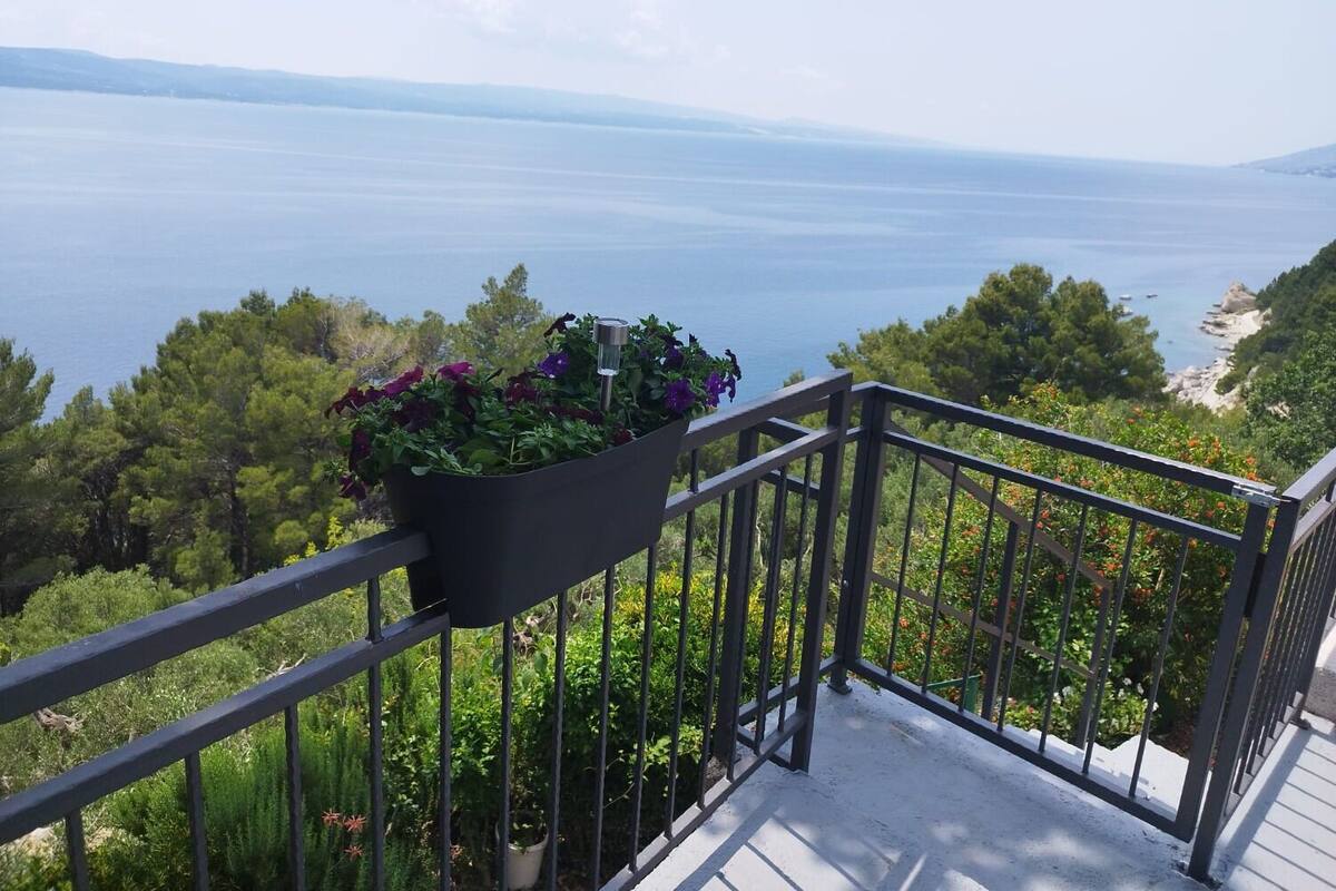 A balcony with a metal railing overlooking a coastal landscape with trees and a view of the sea.
