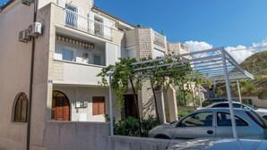 Un edificio de dos plantas con un balcón, cochera y un porche con plantas.