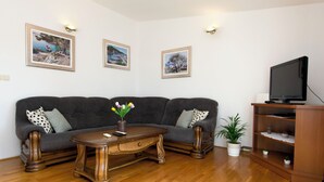 Un salón con un sofá gris oscuro, una mesa de centro de madera y un televisor sobre un mueble de madera. Hay tres cuadros en la pared, una planta en maceta y un pequeño estante con adornos.