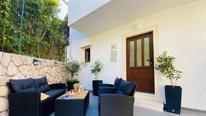 An outdoor patio with black wicker furniture, a stone wall, and potted plants. - Apartment Daria (Postira)