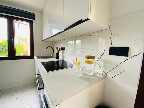 Une cuisine moderne dotée d’un plan de travail noir, d’un pare-feu en marbre blanc et d’une fenêtre donnant sur un paysage verdoyant.
