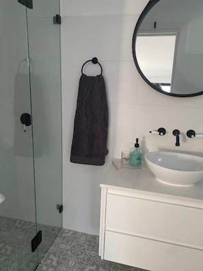 A modern bathroom with a glass shower enclosure, a white vanity with a sink, and a round mirror. - Golf Course & Beach Stay Self-contained Guest House (Nelson Bay)